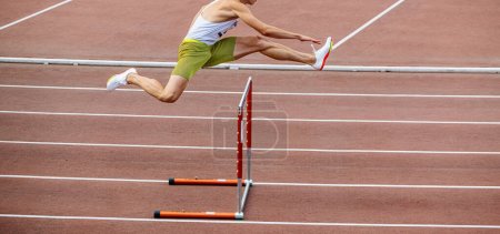 Foto de Male athlete running 400 meters hurdles at stadium - Imagen libre de derechos