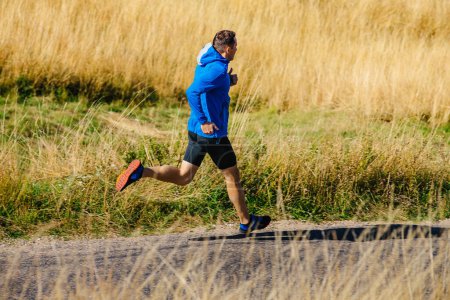 Photo for Male runner running on road among dry grass - Royalty Free Image