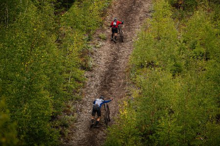 Photo for Back two cyclists climb uphill with mountain bike in trail forest. cross-country cycling competition - Royalty Free Image