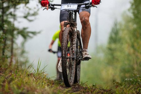 Photo for Athlete cyclist on mountain bike riding uphill in forest front view. feet in drops mud. cross-country cycling competition - Royalty Free Image