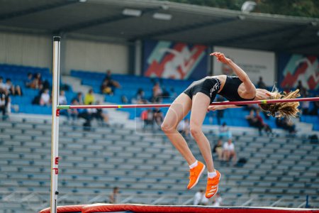 Foto de Mujer joven atleta salto de altura competición de atletismo, zapatos de púas Adidas y pantalones cortos, juegos de deportes de verano - Imagen libre de derechos