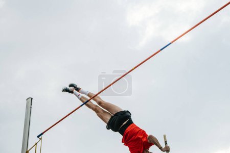 Foto de Espalda macho atleta pole bóveda en el fondo del cielo, zapatos de espigas Adidas para saltar, juegos de deportes de verano - Imagen libre de derechos
