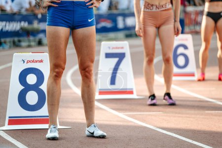 Foto de Piernas grupo de atletas femeninos comienzan a correr carrera de media distancia en el estadio, zapatos de espigas para correr Nike, marcadores de carril polanik - Imagen libre de derechos