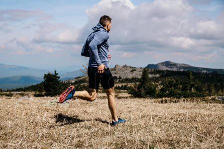 Téléchargez les photos : Homme coureur piste de montagne sur herbe sèche, vue latérale, chemise à manches longues bleue et collants noirs, photo de sport - en image libre de droit
