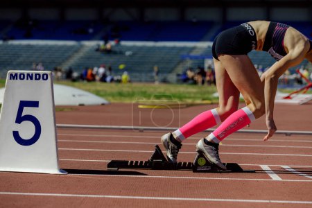 Foto de Velocista femenina corriendo desde bloques de partida en atletismo, ropa de correr Nike y marcadores de carril Mondo, mangas de compresión Compressport - Imagen libre de derechos