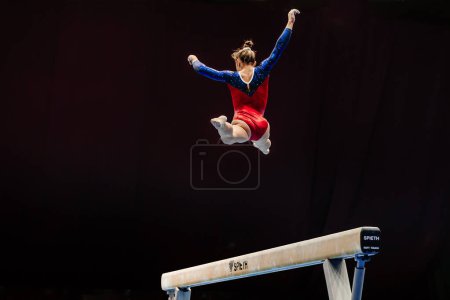 Téléchargez les photos : Femme gymnaste exercice split saut en faisceau d'équilibre sur fond noir, appareil Spieth faisceau d'équilibre, jeux de sport d'été - en image libre de droit