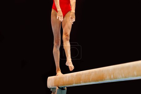 Photo for Legs female gymnast in red swimsuit exercise balance beam gymnastics on dark background, olympic sports included in summer games - Royalty Free Image