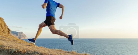 Foto de Corredor masculino corriendo montaña mar sendero sobre hierba marchita, carrera de cross-country - Imagen libre de derechos