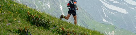 Photo for Male runner run down mountain trail, skyrunning race ultramarathon, green meadows and snow-capped peaks - Royalty Free Image