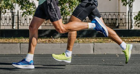 Beine zwei männliche Läufer laufen Stadtmarathon, Sportler joggen auf Asphaltstraße, Sommersportspiele