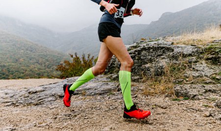 Foto de Atleta femenina en calcetines de compresión corriendo carrera sendero de montaña, trotando en el clima de otoño brumoso a través del terreno montañoso - Imagen libre de derechos