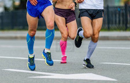 Téléchargez les photos : Trois coureurs athlètes masculins et féminins courent course de marathon, jambes de jogger en chaussettes de compression courir route de la ville - en image libre de droit