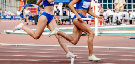 Foto de Equipo de mujeres corriendo carrera de relevos en el estadio de pista campeonatos de atletismo de verano, pasando porra en el escenario - Imagen libre de derechos