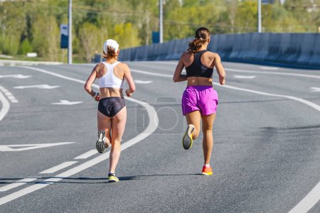 Foto de Espalda dos corredores femeninos que corren en carrera de maratón de paso elevado, competición de deportes de resistencia, atleta jogger mujer - Imagen libre de derechos