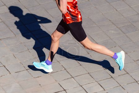 Téléchargez les photos : Athlète coureur vue de dessus course marathon, jogger ombre sur dalles de pavage, kinesiotaping du muscle de veau - en image libre de droit