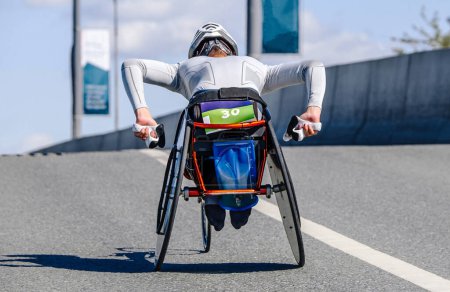 Téléchargez les photos : Para athlète sur route de course en fauteuil roulant, passage supérieur en montée, course de marathon compétition de para athlétisme - en image libre de droit