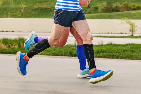 Foto de Piernas dos corredores masculinos en calcetines de compresión y mangas corren distancia maratón, competición deportiva de resistencia - Imagen libre de derechos