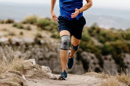 Téléchargez les photos : Coureur masculin avec genouillères sur piste de montagne, manchons de compression protecteurs contre les blessures pour stabiliser les jambes - en image libre de droit