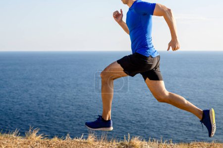 corredor masculino corriendo sendero de montaña en el fondo del mar y el cielo, trotando de verano a lo largo de la costa