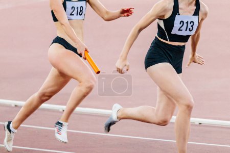 Foto de Mujeres corriendo carrera de relevos en el campeonato de atletismo de verano, pasando batuta dos atletas mujeres - Imagen libre de derechos