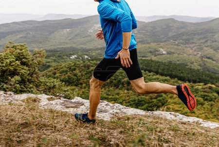 Foto de Corredor masculino en cortavientos y mallas corriendo a lo largo del precipicio, hombre corredor atleta correr sendero de montaña - Imagen libre de derechos