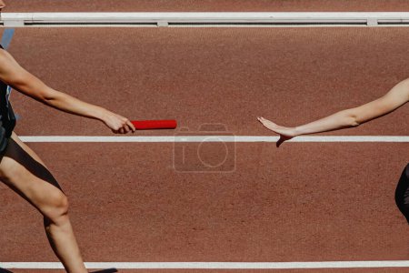Téléchargez les photos : Coureuse de main passant le relais de course de bâton dans la compétition d'athlétisme d'été - en image libre de droit