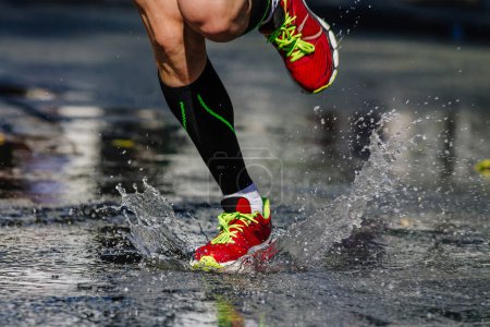 Foto de Piernas atleta corredor en calcetines de compresión corriendo charco en la carretera, carrera de maratón de verano - Imagen libre de derechos