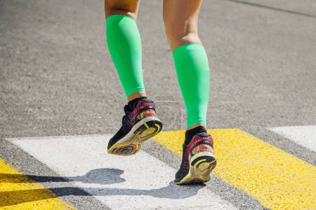 Téléchargez les photos : Jambes coureur féminin en vert vif chaussettes de compression courir passage piéton sur la route - en image libre de droit