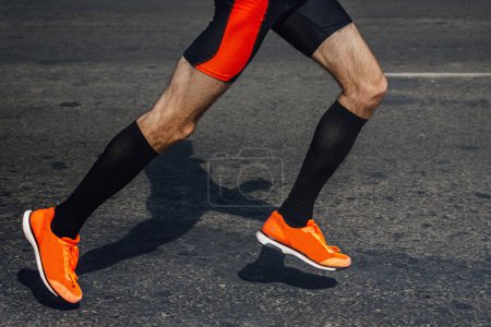 Photo for Legs male runner in black compression socks and bright running shoes, shadow man jogger in dark asphalt - Royalty Free Image