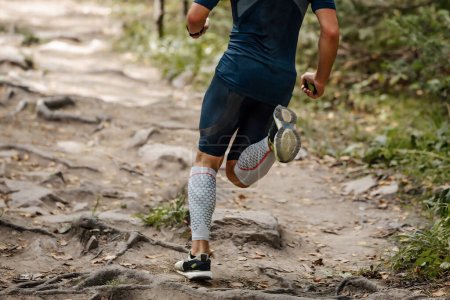 Foto de Corredor atleta espalda en mangas de compresión en sus pies sendero bosque corriendo, carrera de maratón de verano - Imagen libre de derechos