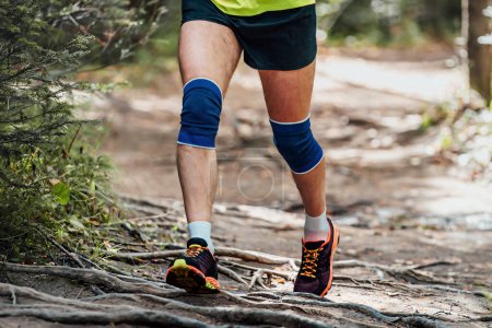 Photo for Male runner in knee pads running forest trail on tree roots, summer marathon race - Royalty Free Image