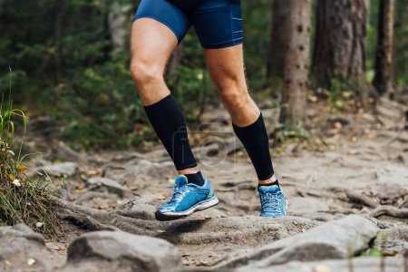 Foto de Piernas corredor en mangas de compresión en sus pies carrera sendero bosque sobre piedras, carrera maratón de verano - Imagen libre de derechos
