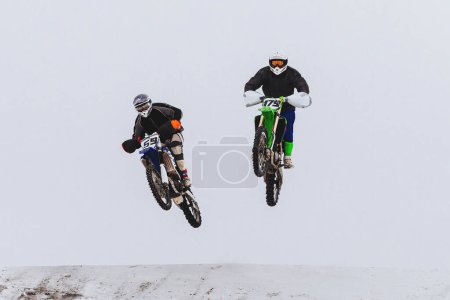 Foto de Dos motocross rider saltando juntos en el trampolín nevado, carreras de motos todo terreno de invierno - Imagen libre de derechos