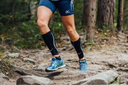 Foto de Corredor masculino correr maratón de sendero forestal en mangas de compresión Mizuno, mallas y zapatillas de running Asics - Imagen libre de derechos