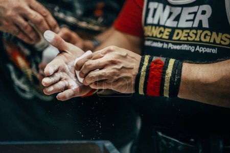 Photo for Athlete powerlifter apply gym chalk on his hands for bench press. Singlet and wrist wraps Inzer - Royalty Free Image