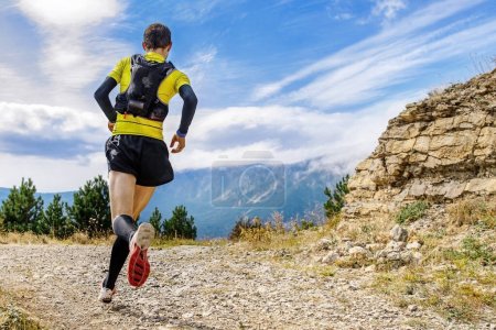 Foto de Vista trasera corredor masculino con camelback y calcetines de compresión corriendo carrera maratón de montaña - Imagen libre de derechos