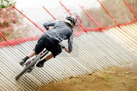 Photo for Rear view mountainbiker rips turn on wood insloped corner in downhill race, summer extreme sports - Royalty Free Image