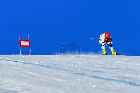 Foto de Corredor de esquí en la pista de esquí alpino cuesta abajo, puerta roja y la pendiente nevada sobre fondo cielo azul, juegos de deportes de invierno - Imagen libre de derechos