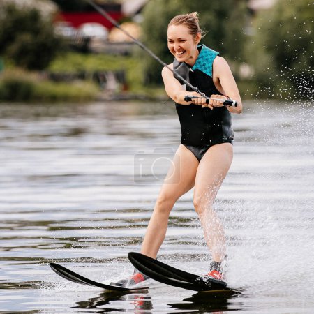 Téléchargez les photos : Souriant jeune femme ski nautique derrière bateau à moteur sur étang, vacances d'été joie - en image libre de droit