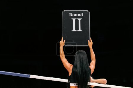 Photo for Brunette ring girl demonstrate sign with number round 2 during fight MMA on dark background - Royalty Free Image