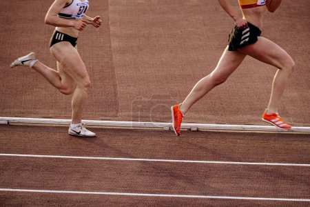 Photo for Two female runner in Nike and Adidas spikes shoes middle-distance running at stadium in summer athletics championships - Royalty Free Image