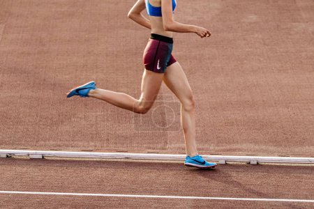 Foto de Joven corredora en zapatillas Nike Spikes y pantalones cortos de media distancia corriendo en el estadio en campeonatos de atletismo de verano - Imagen libre de derechos