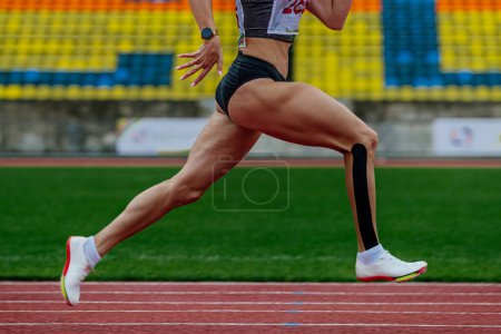 Foto de Primer plano corredor hembra corredor pista de atletismo estadio, campeonatos de atletismo de verano, kinesiotaping en la pierna inferior - Imagen libre de derechos