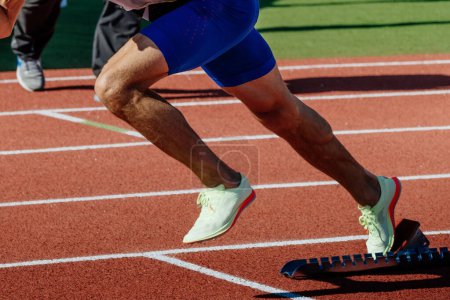 Foto de Close-up piernas corredor masculino corriendo en bloques de partida carrera de sprint, campeonatos de atletismo de verano - Imagen libre de derechos