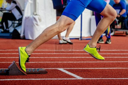 Téléchargez les photos : Gros plan athlète masculin commencer à courir dans les blocs de départ course de sprint, championnats d'athlétisme d'été, chaussures à pointes jaune vif - en image libre de droit