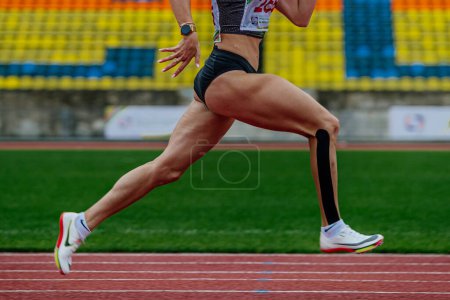 Foto de Corredor hembra sprinter pista de atletismo estadio en zapatos Nike Spikes, campeonatos de atletismo de verano, kinesiotaping en la parte inferior de la pierna - Imagen libre de derechos