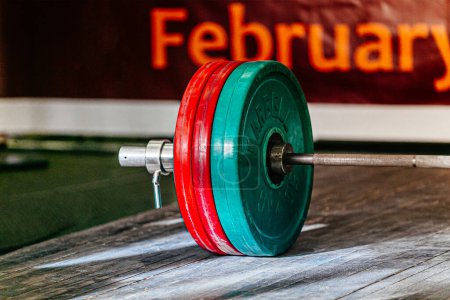 Photo for Close-up barbell with red and green plates on wooden platform at powerlifting competition - Royalty Free Image