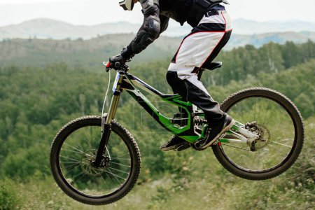Foto de Atleta ciclista cuesta abajo saltando en el bosque de fondo y las montañas, campeonato de verano mountainbike - Imagen libre de derechos