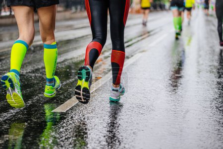 Foto de Piernas dos mujeres zapatillas de correr Asics carrera maratón en carretera mojada, calcetines de compresión Compressport - Imagen libre de derechos