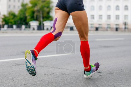 Téléchargez les photos : Jambes athlète coureuse marathon de course en ville, chaussettes de compression sur les pieds, kinésiotaping sur les genoux pour la prévention - en image libre de droit